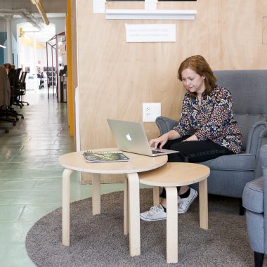 Mujer sentada en un sillón, trabajando en su portátil. Está en un coworking dog friendly.